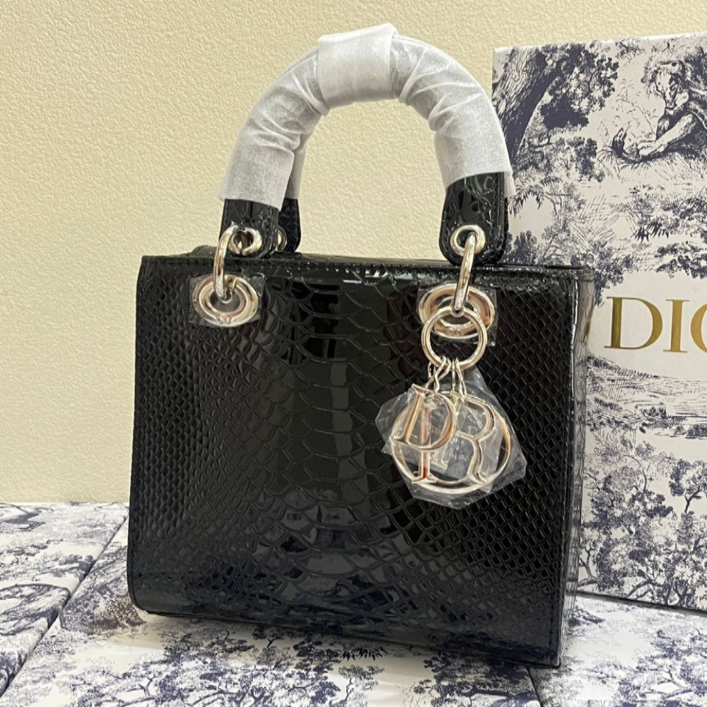 Black handbag with white handle and Dior keychain on a patterned surface with Dior box in the background.