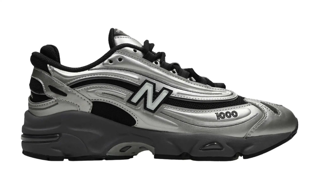 New Balance 1000 unisex sneaker with metallic silver overlays, black mesh-style panels, a large N side logo and a sculpted grey sole