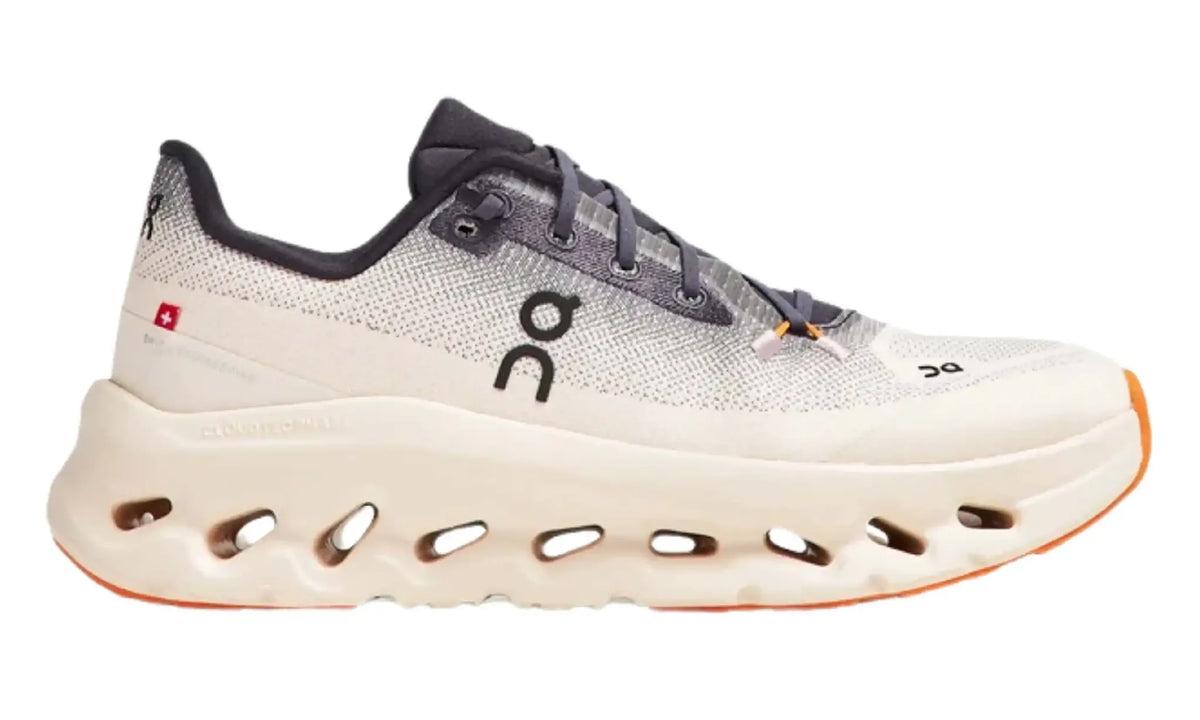Side view of On Cloudtilt Iron/Dew women's sneakers with cream upper, dark laces and orange sole accents