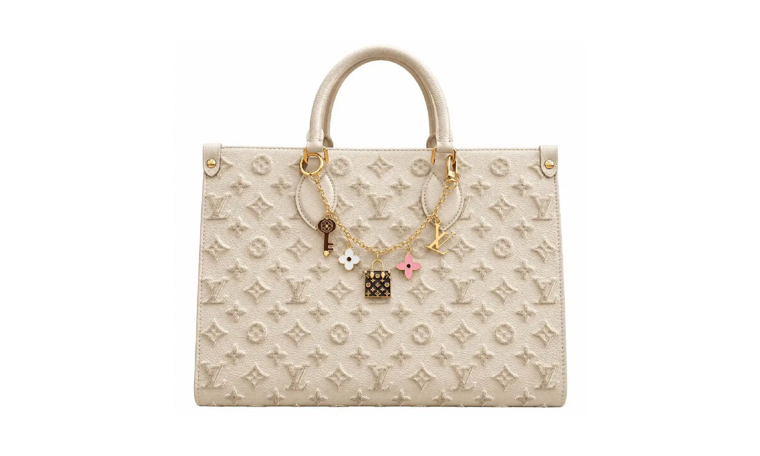Front view of Cream OnTheGo MM monogram tote bag with gold-tone charm chain and top handles