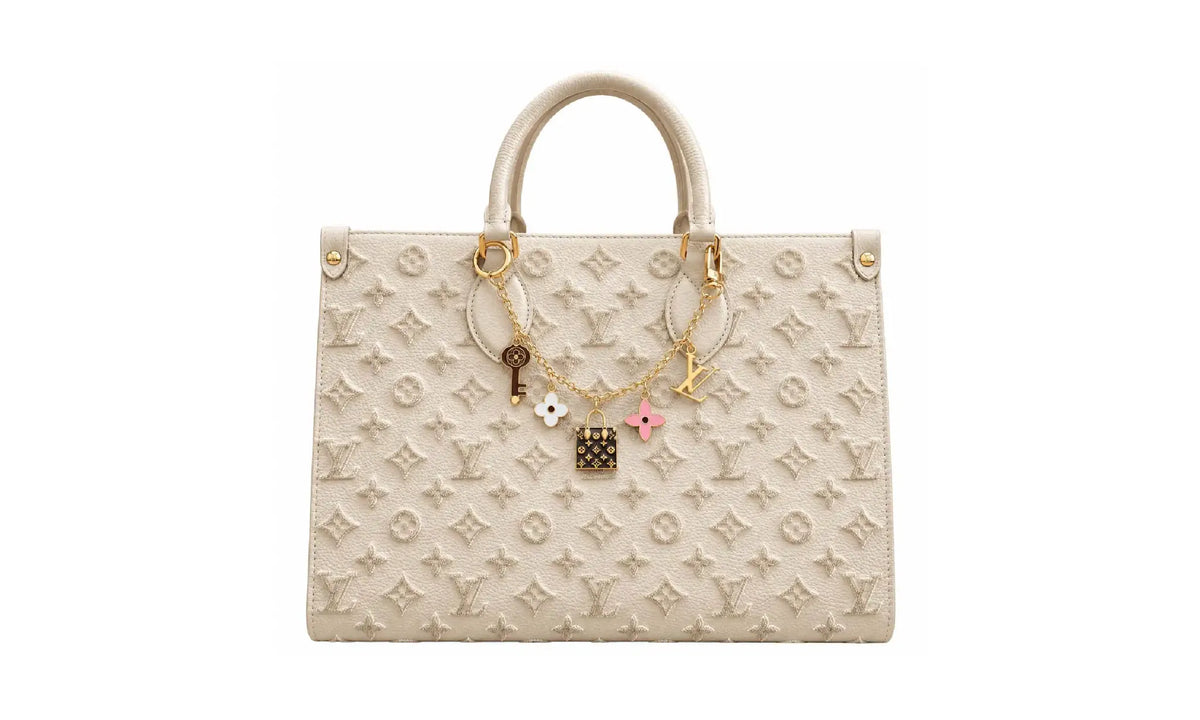 Front view of Cream OnTheGo MM monogram tote bag with gold-tone charm chain and top handles